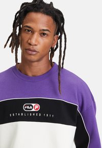 Felpa girocollo viola e nera con accenti bianchi. Presenta il logo "Fila" e la scritta "Established 1911" sulla parte anteriore. Materiale in misto cotone.