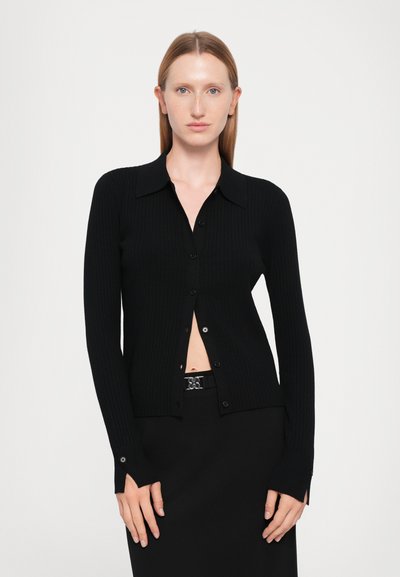 Black ribbed cardigan with a collared neckline, button closure, and long sleeves. Paired with a black skirt featuring a decorative belt.