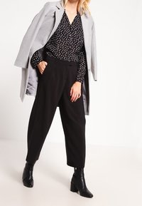 Jasnoszary płaszcz noszony na czarną koszulę z guzikami i białymi wzorami serc, w połączeniu z czarnymi spodniami o wysokim stanie i czarnymi botkami na obcasie.