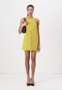 Yellow sleeveless mini dress with a front zipper detail, paired with a black shoulder bag and black high-heeled shoes. Smooth texture.