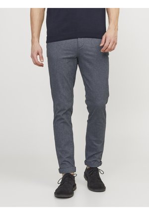 Pantalons gris à motif en tissu tissé avec une coupe slim, présentant des ourlets retroussés, portés avec des chaussures noires et un pull bleu marine.