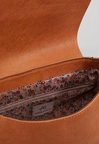 Brązowa torebka z ekologicznej skóry z podszewką w kwiatowy wzór. Wewnątrz znajduje się kieszeń na zamek, umożliwiająca dodatkowe przechowywanie i organizację.