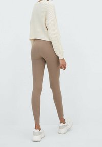 Leggings de canalé beige combinados con un suéter de punto grueso color crema, de diseño corto y mangas largas, llevados con zapatillas blancas.