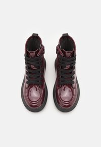 Burgundy patent leather ankle boots with black laces, featuring a textured lining and a thick black rubber sole. Zipper detail on the side.