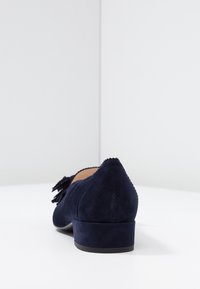 Marineblauw suède schoen met een lage hak, ronde neus en decoratieve franjes; heeft golvende randen langs de opening van de schoen.