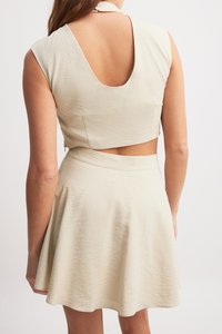 Costum în două piese de culoare crem, compus dintr-un top scurt cu spate adânc și o fustă evazată. Materialul are un finisaj texturat cu un model subtil.
