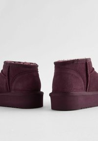 Bottines bordeaux en suède doux avec doublure intérieure en peluche, semelle plate et coutures renforcées le long des seams.