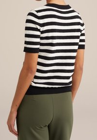 Svart och vit randig kortärmad tröja med texturdetaljer, ribbad halsringning och nederkant, ihop med gröna byxor.