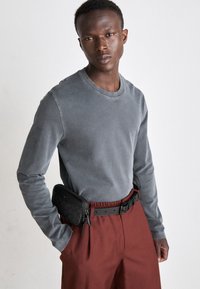 Långärmad grå bomullsskjorta, kombinerad med högmidjade rustfärgade byxor. Ett smalt svart bälte och en liten svart väska kompletterar outfiten.