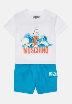 Camiseta blanca de algodón con gráfico de oso colorido y pantalones cortos azules con un bolsillo lateral y etiqueta "MOSCHINO". Diseño suave y casual.