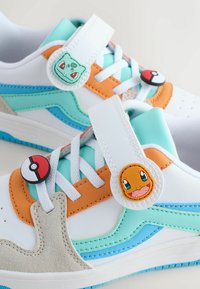 Beli supergi vsebujejo večbarvne poudarke v turkizni, oranžni in sivi barvi. Poudarki vključujejo gumbe z motivi in teksturirane prekrivke na straneh.