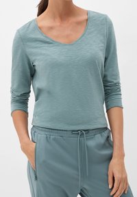 Helles blaues Langarmshirt mit einem V-Ausschnitt und strukturierter Stoffqualität, kombiniert mit passenden Jogginghosen mit Kordelzug und seitlichen Taschen.