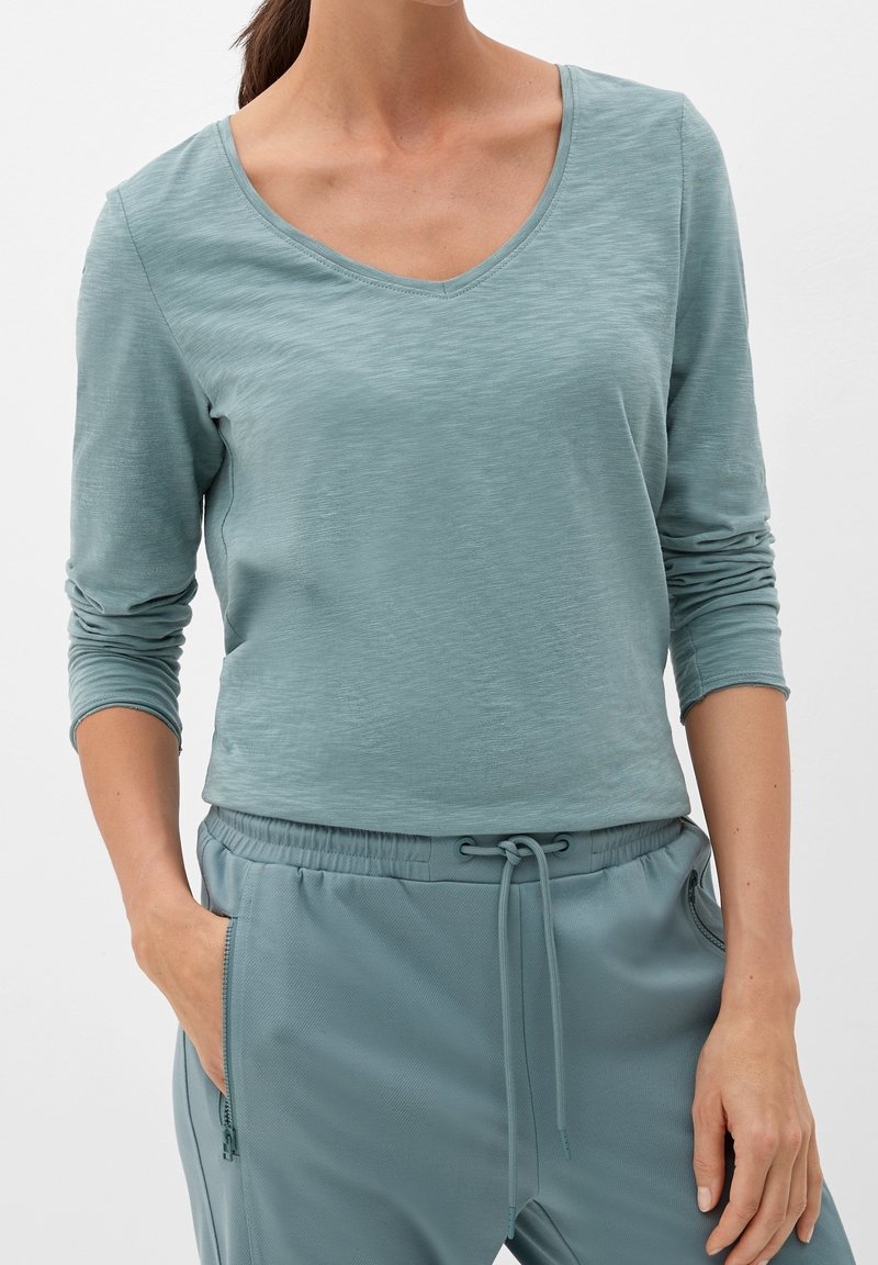 Helles blaues Langarmshirt mit einem V-Ausschnitt und strukturierter Stoffqualität, kombiniert mit passenden Jogginghosen mit Kordelzug und seitlichen Taschen.