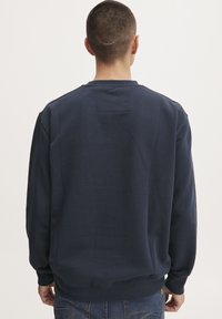 Sudadera marina con cuello redondo, mangas largas y un acabado texturizado. Presenta un pequeño parche en la parte posterior cerca del cuello.