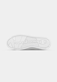 White sneaker sole featuring a textured grip pattern and a prominent logo, with herringbone and circular tread designs for traction.