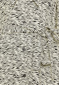Gros plan sur une robe à imprimé zèbre noir et blanc avec une ceinture en tissu nouée et des boutons noirs sur le devant.