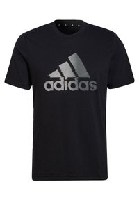 Musta puuvillapaita, jossa on suuri, teksturoitu hopeinen Adidas-logo rinnassa. Klassinen pyöreä kaula-aukko, lyhyet hihat, normaali istuvuus.