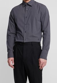 Černobíle vzorovaná košile na knoflíky s herringbonovým designem, se standardním límcem a dlouhými rukávy, doplněná černými kalhotami.