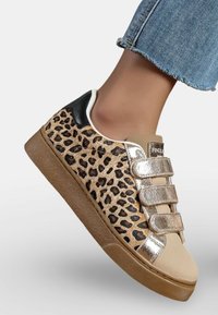 Baskets à imprimé léopard beige avec des straps Velcro métalliques dorés, accent noir au talon et semelles en caoutchouc. Détail texturé de l'imprimé animal.