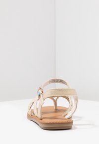 Beige-nauhat sandaalit, joissa on tasapohja, kangasremmit ja vaaleanruskea pohja. Koristeltu turkoosilla yksityiskohdalla ja säädettävällä soljella.