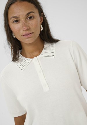 Polo de punto blanco de manga corta con cierre de botones en la parte delantera y un cuello adornado con pequeños botones metálicos para añadir textura y detalle.