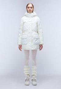 Hvid oppustelig jakke med hætte, frontlommer og en glat tekstur. Båret med lyse leggings og kraftige, strikkede benvarmere.