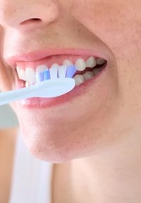 Tandenborstel met zachte haren, in blauw en wit, geplaatst nabij heldere, gezonde tanden in een close-upweergave.