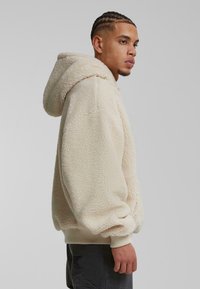 Felpa con cappuccio di colore crema, dal tessuto morbido, con vestibilità oversize e cappuccio foderato. Polsini e orlo a costine, con un motivo di cucitura unico.