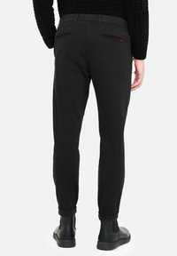 Black trousers with a slim fit, featuring a smooth texture, two back zip pockets, and rolled cuffs, paired with black ankle boots.