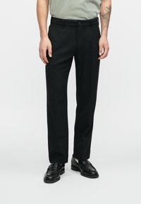 Pantaloni neri su misura con una vestibilità dritta, passanti per cintura e chiusura con zip. Tessuto liscio con una lucentezza sottile, abbinato a scarpe eleganti nere.