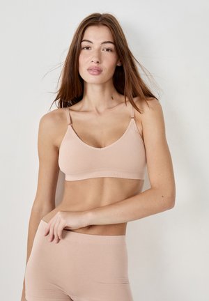 Nude naadloze bralette met verstelbare bandjes, zachte stof en een comfortabele pasvorm, gecombineerd met bijpassende nude naadloze shorts.