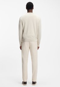 Hellbeiger Pullover mit langen Ärmeln, gerippten Bündchen und Saum, kombiniert mit passenden hellbeigen Hosen und dunklen Schuhen. Glatter Stofftextur.