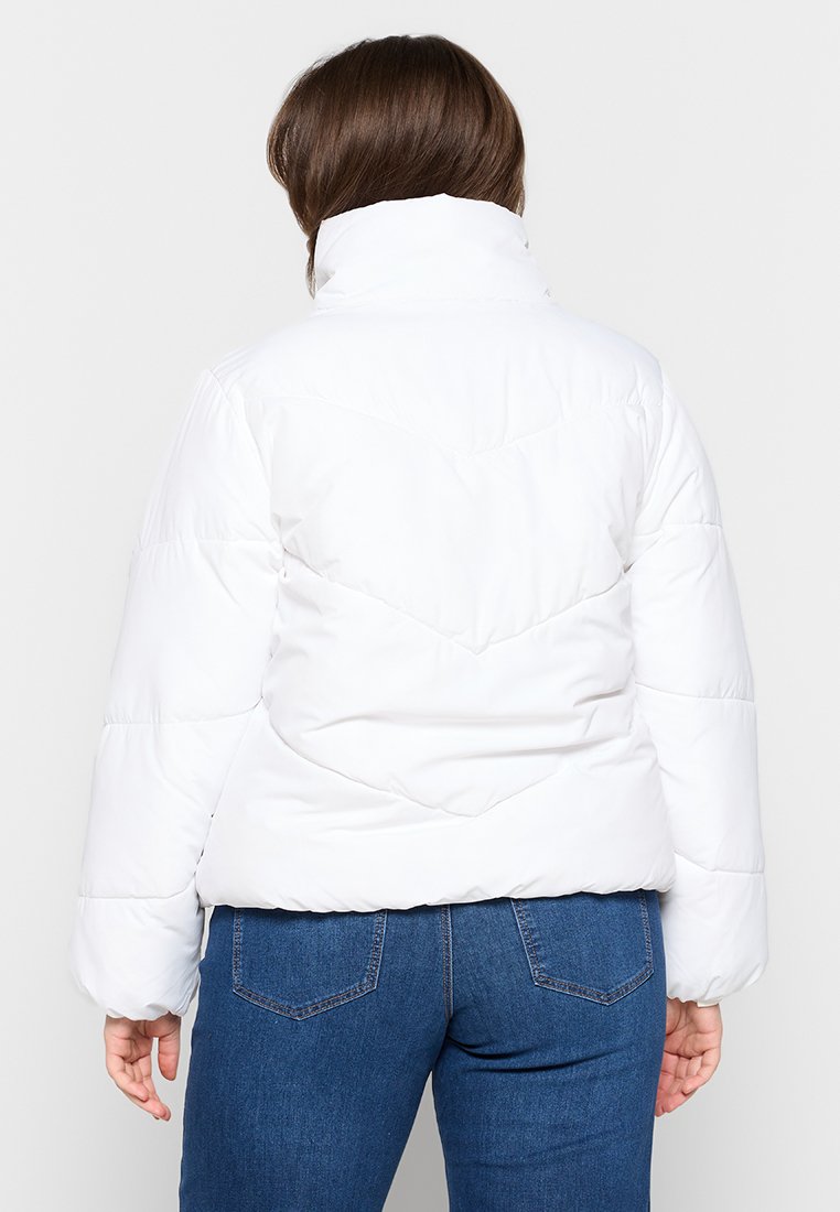 Witte pufferjack met een hoge kraag, gewatteerd ontwerp en een chevronpatroon op de rug. Gekocht met blauwe spijkerbroeken.