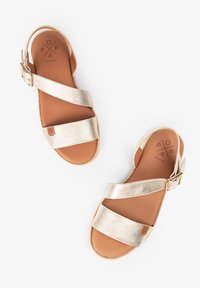 Sandalias metálicas doradas con tiras cruzadas, cierre de hebilla y plantilla color tostado. Presentan tiras texturizadas y un pequeño logo cerca de la parte inferior.
