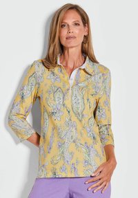 Gele poloshirt met een paisley- en bloemenpatroon, voorzien van een witte kraag en driekwart mouwen. Zachte stoftextuur.