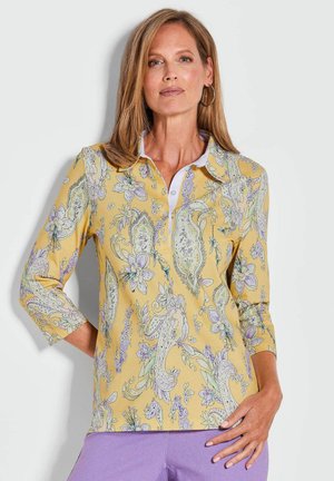 Polo jaune avec un motif paisley et floral, doté d'un col blanc et de manches trois-quarts. Texture de tissu douce.
