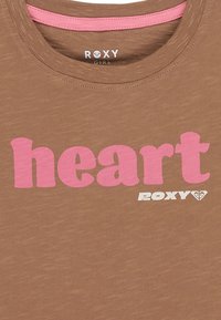 Hnědé tričko s krátkým rukávem a kulatým výstřihem; na dolním pravém rohu velký růžový nápis "heart" a logo Roxy v bílé barvě. Měkká textura.