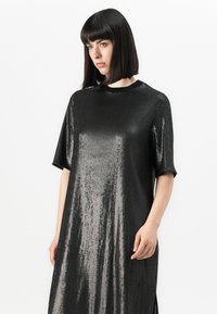 Abito nero a maniche corte realizzato in tessuto lucido e strutturato. Vestibilità ampia, lunghezza al ginocchio, con scollo tondo e spacchi laterali.