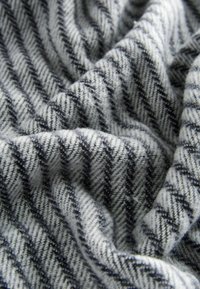 Grau-weißes Hahnentritt-Muster auf Stoff, der eine weiche Textur mit gewebten Streifen zeigt und in sanften Falten hängt.