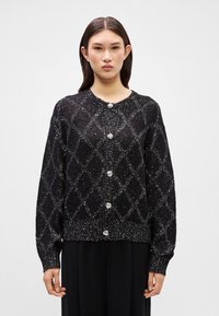 Black cardigan with a diamond pattern and metallic shimmer. Features five silver buttons, ribbed cuffs, and a round neckline. Soft texture.