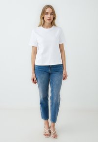 Witte katoenen t-shirt met korte mouwen, voorzien van subtiele versieringen, gecombineerd met lichtblauwe denim jeans en witte, strap sandalen.