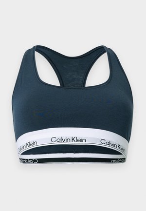 Donkerblauwe racerback sportbeha met witte elastische band waarop herhaaldelijk het "Calvin Klein"-logo in het zwart staat.