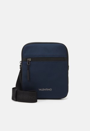 Sac bandoulière marine en tissu texturé, avec bord noir, poche zippée à l'avant et sangle ajustable arborant un logo en relief. Design compact et rectangulaire.