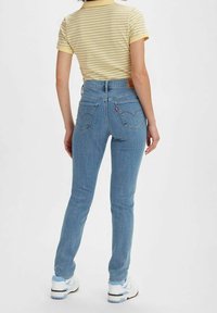 Jean en denim bleu taille haute avec une coupe slim, comportant des poches arrière et une étiquette en cuir. Associé à un polo à rayures jaunes.