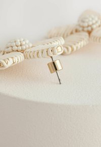 Gold-tone metal knob with a textured white woven design. Features round bead accents, enhancing the intricate detailing.