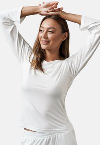 Biała longsleeve koszula wykonana z gładkiego materiału, o luźnym kroju. Posiada okrągły dekolt i miękką, płynącą fakturę. Prosty i minimalistyczny design.