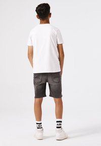 Witte short-sleeve t-shirt, grijze denim shorts, witte sneakers en zwart-witte gestreepte sokken. Casual outfit weergegeven van achteren.