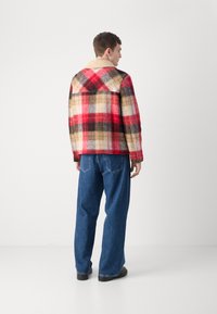Plaid wool coat in red, black, and beige tones with a tan collar; paired with loose blue denim jeans and black shoes, viewed from behind.