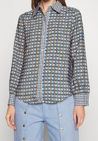 Camicia a maniche lunghe con bottoni in un motivo geometrico multicolore con una palette di blu, marrone e bianco; presenta un colletto e dei polsini patterned.