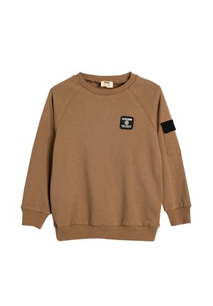 Brązowy sweter z okrągłym dekoltem, ściągaczami na rękawach i u dołu. Posiada czarną łatę z napisem na piersi oraz czarny akcent na rękawie.